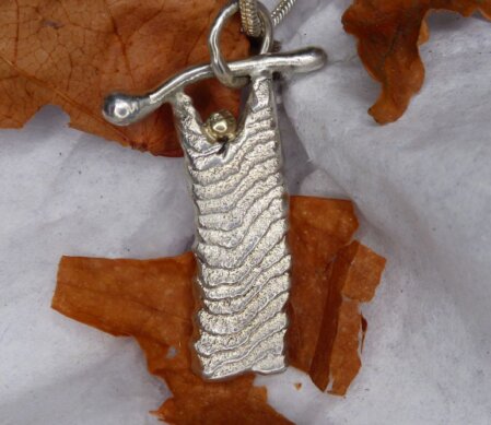 Anhaenger, schmale-laengliche Form. Unterschiedliche Struktur auf Vorder- und Rueckseite. Max. Maße: 16 x 25mm